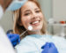 Image of satisfied young woman sitting in dental chair at medical center while professional doctor fixing her teeth
